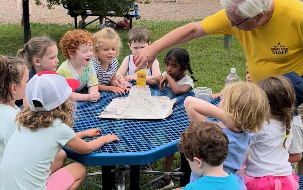 an adult male counselor assisting a group of young kids during a day camp activity