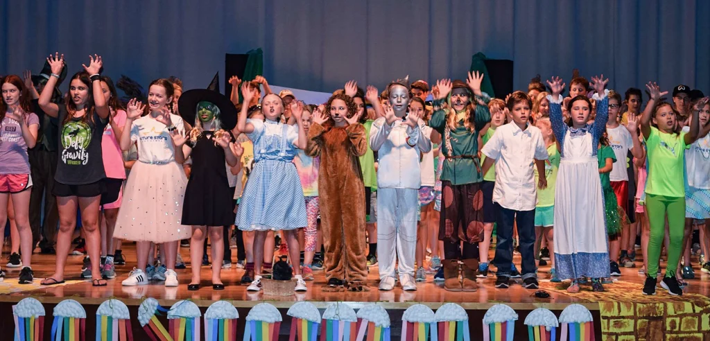 a group of young kids performing on a stage during a camp program that fosters their confidence and indepdence.