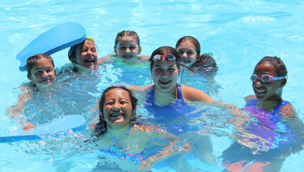 a group of young girls in a bright blue pool on a sunny day