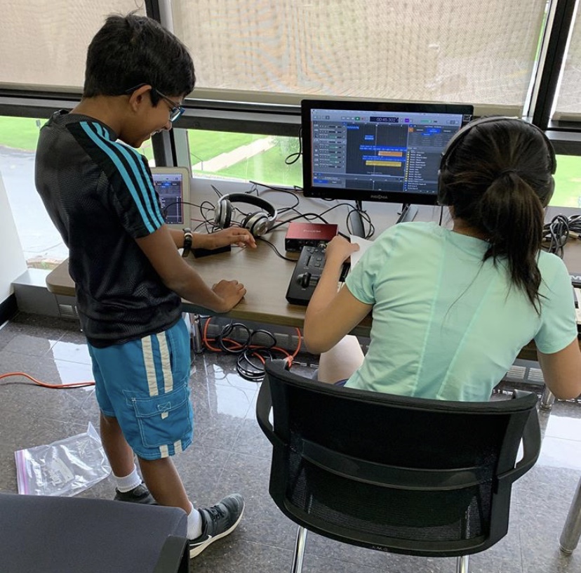 two young kids sitting at a table with electronic gadgets and a computer